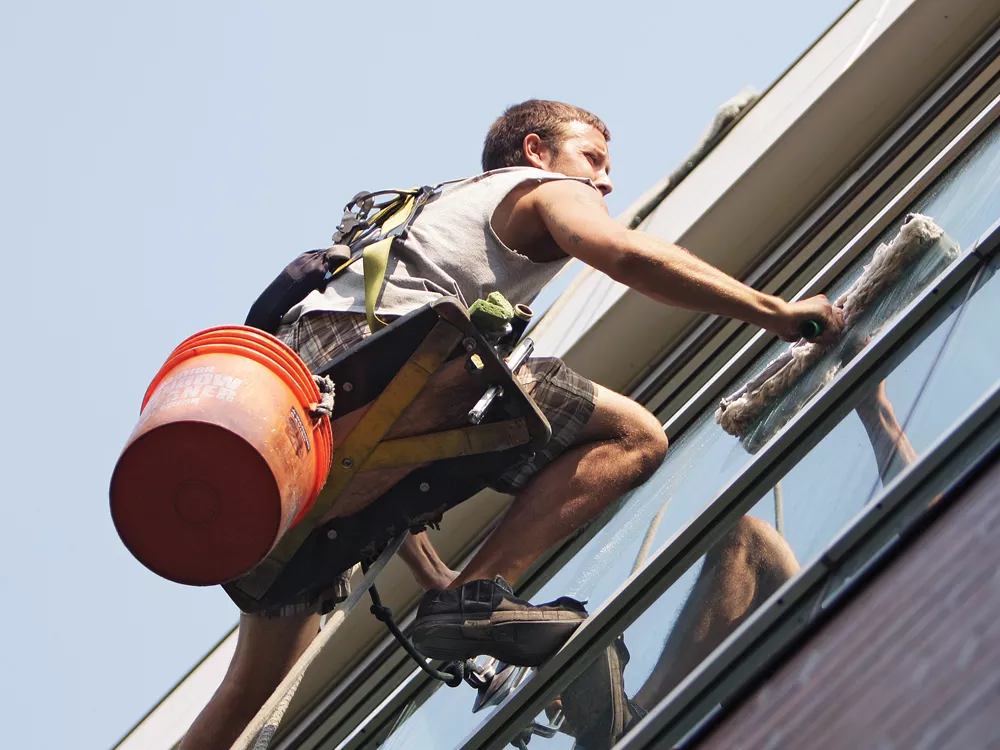 West Coast Window Cleaning employee John Peterson clings to the side of the Spokane Arena. - YOUNG KWAK