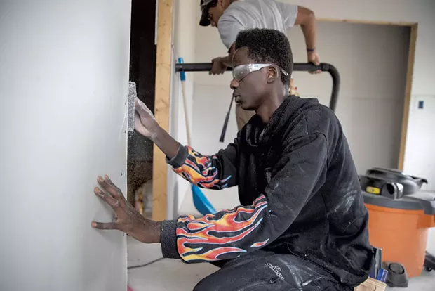 Essex High School senior Mustaf Mohamed uses a surform rasp to make drywall flush with a door frame - JAMES BUCK
