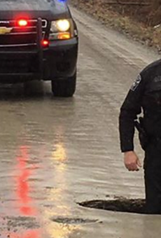 A Grand Blanc Township police officer stands knee-deep in a pot hole on McWain Road.
