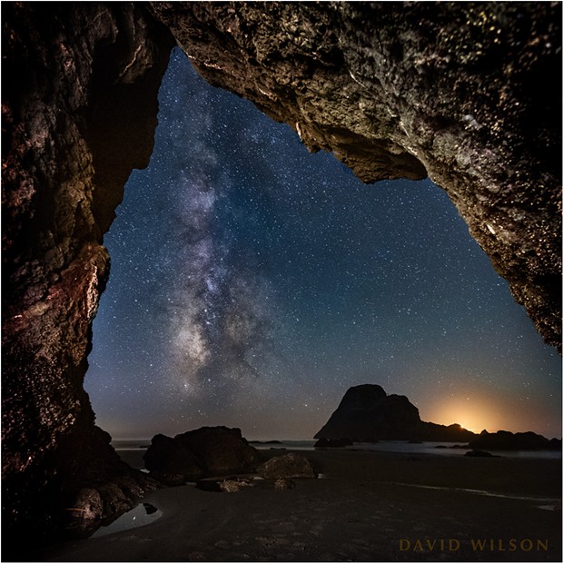 The Milky Way rises from the horizon near the glow of the setting crescent moon outside of this hidden Houda Beach cave. Camel Rock’s silhouette is large on the horizon beside the glow of the setting crescent moon. Humboldt County, California. September 13, 2018. - DAVID WILSON