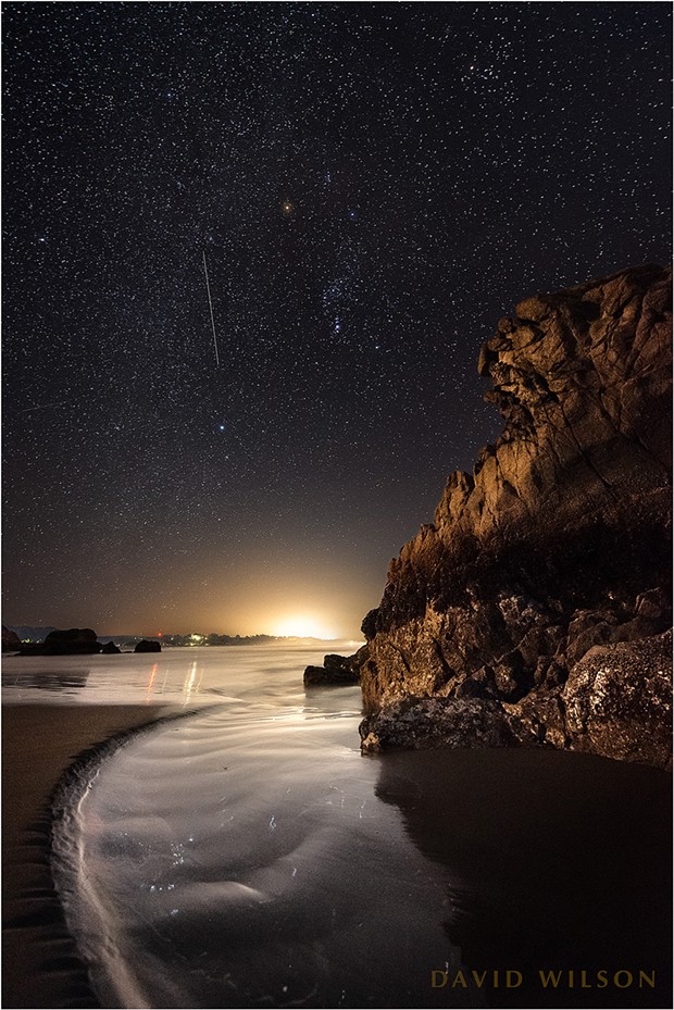 Lights from shore illuminate this great chunk of rock here where the wild coastline intersects with humanity. Above, a satellite’s eye in the sky so high crawled slowly past Orion. Humboldt County, California. February 22, 2019. - DAVID WILSON