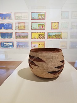 An early 20th-century Karuk basket in front of paintings by Lyn Risling. - PHOTO BY GABRIELLE GOPINATH