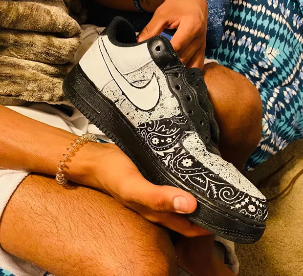 The kid holds one of the shoes he paints in a makeshift art studio in the backyard of his great aunt's house on Howard Street. - PHOTO BY ASHLEY HARRELL