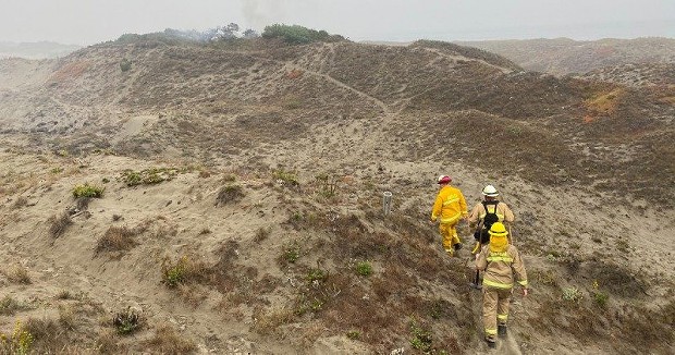 Firefighters hiking to the incident while smoke rises over a dune. - PHOTO BY TED MCNAMEE