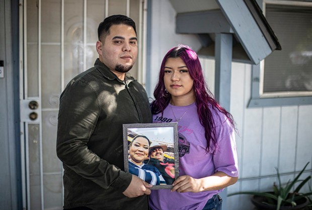 Martin (left) and her sister Miranda Basulto (right) pose with a framed portrait of their parents for a photo in front of their home in Coalinga on June 28, 2022. Miranda is eligible for a state bond given to kids who lost a caregiver (or both) because of COVID. - PHOTO BY LARRY VALENZUELA, CALMATTERS/CATCHLIGHT LOCAL