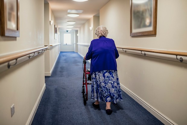 A senior woman walking down a corridor with the assistance of a walker. view from rear - ISTOCK