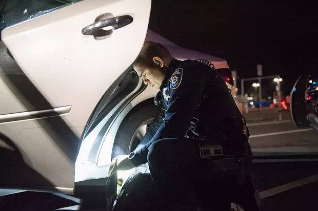 EPD officer Raymond Nunez searches a backpack in the WinCo parking lot. - PHOTO BY MARK MCKENNA