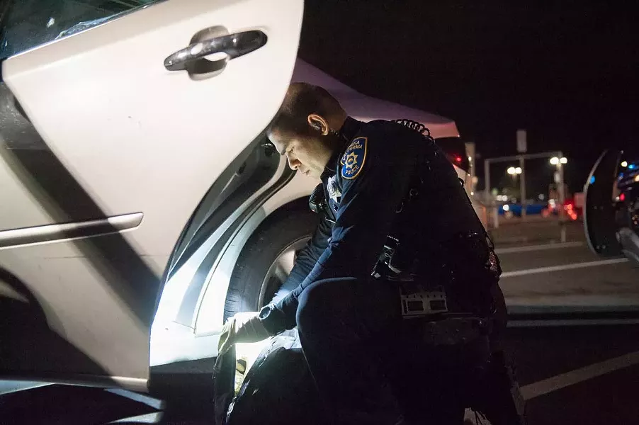 EPD officer Raymond Nunez searches a backpack in the WinCo parking lot. - PHOTO BY MARK MCKENNA