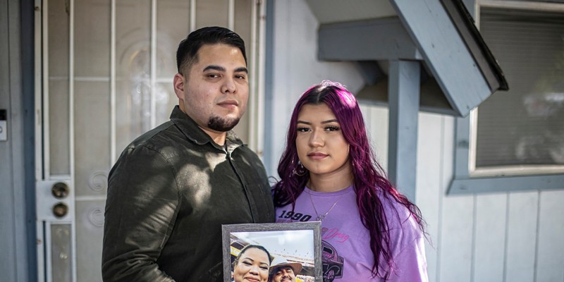 Martin (left) and her sister Miranda Basulto (right) pose with a framed portrait of their parents for a photo in front of their home in Coalinga on June 28, 2022. Miranda is eligible for a state bond given to kids who lost a caregiver (or both) because of COVID.