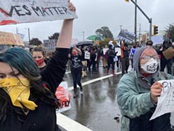 ZACH LATHOURIS - Protesters with masks and signs make their way down rainy streets Saturday, May 30.