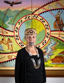 PHOTO BY DAVE WOODY - Lyn Risling with her 2019 mural "We Are These People" in the Native American Forum at Cal Poly Humboldt.