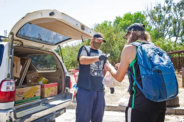 A HELPING HAND Paul Andreano, a volunteer with Hope's Village of SLO, hands out food to people living near the Bob Jones Trail, a popular homeless camp. - FILE PHOTO BY JAYSON MELLOM
