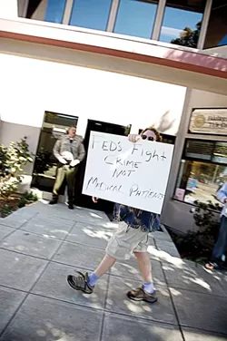 ONE-MAN PROTEST : As law enforcement agents wrapped up a raid in March 2007, Kent Connela paced the sidewalk with his homemade sign. “You guys are no better than a gang,” he said. “Waste of taxpayers’ money, man.” - FILE PHOTO