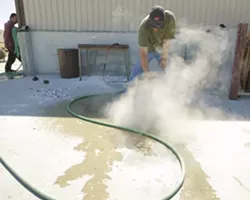 John Kemple sprays the mold with water to break away the plaster mixture from the bronze. This process can be done within minutes of pouring the molten metal into the mold. - PHOTO BY STEVE E. MILLER