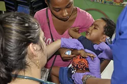 NOT FUN: A mother holds her child close while Dr. Shadi Lanham (pictured), Dr. Rasha Aurshiya, and med student Afsha Aurshiya check the dark-colored spots on his skin. Waves of Health treated more than 1,200 patients during five days of clinics. - PHOTO BY CAMILLIA LANHAM