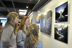 INSPIRED: Alisha Ostby, Olivia Essen, and Gigi Greene check out Burkard’s photos. Essen said before she saw his photography, she thought anyone could take a good photo. “It’s amazing, quite honestly, he’s one of the photographers that pushed me into looking deeper into photography,” she says. - PHOTO BY CAMILLIA LANHAM