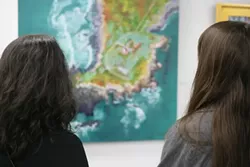 A COUPLE OF LOOKERS : Two of the dozens of opening reception attendees soak in Alyce Broome’s “Lighthouse Peninsula,” a gorgeous aerial view painting. - PHOTOS BY GLEN STARKEY