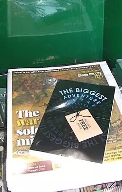 MYSTERY PACKAGE : The Biggest Adventure in the Littlest World, a children’s book by one M.K. Fowler, has been turning up in public places—like this stack of New Times—bearing the charming label “this is a free book.” - PHOTO BY ASHLEY SCHWELLENBACH