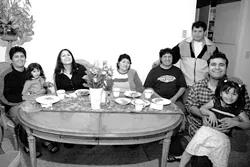 A TABLE TURNED : The Cerron family, whose house on San Luis Obispos Broad Street burned down in February, gather around their new dining room table, one of several pieces of furniture they received from Claudia Goff. (From left, Efrain Cerron with daughter Rochelle in lap, Betzabeth Cerron, Amanda Cerron, Hector Cerron, Fotunato Cerron (standing), Carlos Erazo, and Jade Cerron, in lap.) - PHOTO BY JESSE ACOSTA