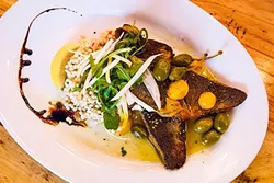 WATER’S FINE : Lively Branzino (Mediterranean sea bass) is lightly pan fried and rested over Israeli couscous bursting with a zesty tabouli of lemon, red onion, tomato, caper berries, tomatoes, and olives. - PHOTO BY JAYSON MELLOM