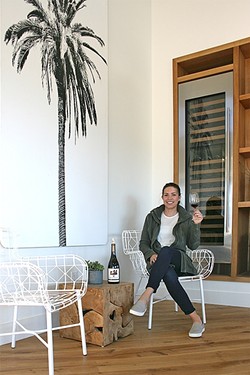 MEET ME UNDER THE PALM:  Biddle Ranch Vineyard General Manager Leigh Woolpert raises a glass of earthy pinot noir to the year ahead among the graphic palm tree d&eacute;cor, which adds a splash of quirk to the Edna Valley tasting room. - PHOTO BY HAYLEY THOMAS CAIN