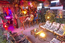 ISLAND TIKI PARTY Kim Tiki (behind the bar) enjoys a laugh with friends at her outdoor tiki bar, a tropical paradise decorated with swap-meet finds and repurposed items saved from the landfill. - PHOTO BY JAYSON MELLOM