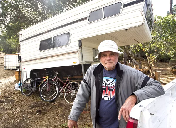 HOME William Carlyle, 76, stands in front of a trailer on his vacant lot in Cambria. He lost his home in the Santa Margarita Hill Fire last June, and he now faces penalties from SLO County for code violations. - PHOTO BY JAYSON MELLOM