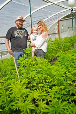 FAMILY FARM Austen Connella (left) and Kristin Kordich (right) pose in front of their Suey Creek cannabis farm with their 3-year-old daughter. - PHOTO BY JAYSON MELLOM