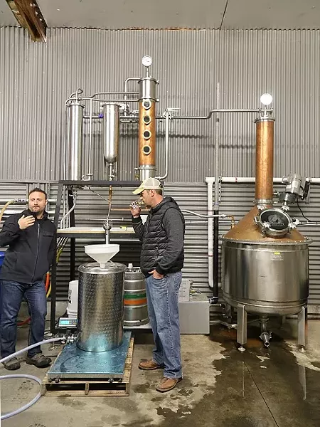 QUALITY CONTROL: Stephen Kroener, left, talks about the intricacies of the distillation process as Joe Barton, right, takes a whiff of their distilled brandy. The two, who are both winemakers, make gin and whiskey at their aptly named distillery Krobar. - PHOTO BY DYLAN HONEA-BAUMANN