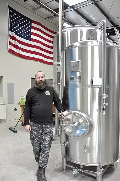 BUILT TO SUIT: Dunbar Brewing’s Chris Chambers designed his new 10-barrel brewhouse, which was built by Paso Tank and Steel. The brite tank he’s standing next to came out of Vancouver, Wash., and came complete with an American flag welded onto the side of it. Marks Metalworks added it specifically for Chambers, a veteran. - PHOTO BY CAMILLIA LANHAM