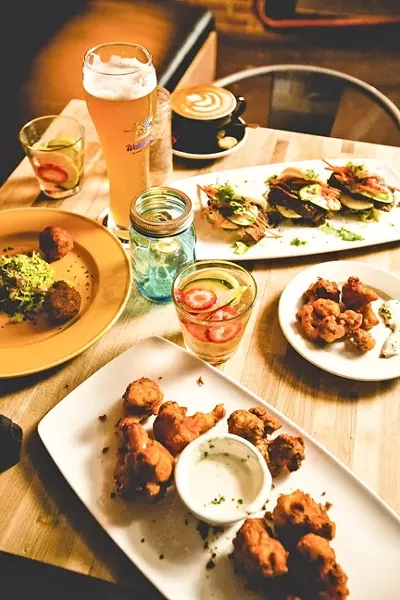 MORE THAN MEETS THE EYE: (Clockwise from top) Frosty beer, freshly-brewed cappuccino, bao pork belly sliders, vegan hot wings, white wine sangria, more hot wings with house-made vegan blue cheese dipping sauce, and parmesan pepper risotto balls, pictured. Everything you see here (except for the coffee, which is available at the Kreuzberg coffee counter) is served up at Kreuzberg’s new lounge area, which springs to life after 6 p.m. Wednesday through Saturday. - PHOTO BY HENRY BRUINGTON