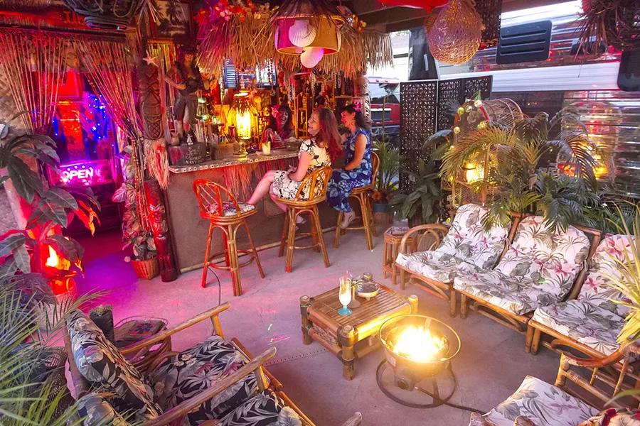 ISLAND TIKI PARTY Kim Tiki (behind the bar) enjoys a laugh with friends at her outdoor tiki bar, a tropical paradise decorated with swap-meet finds and repurposed items saved from the landfill. - PHOTO BY JAYSON MELLOM