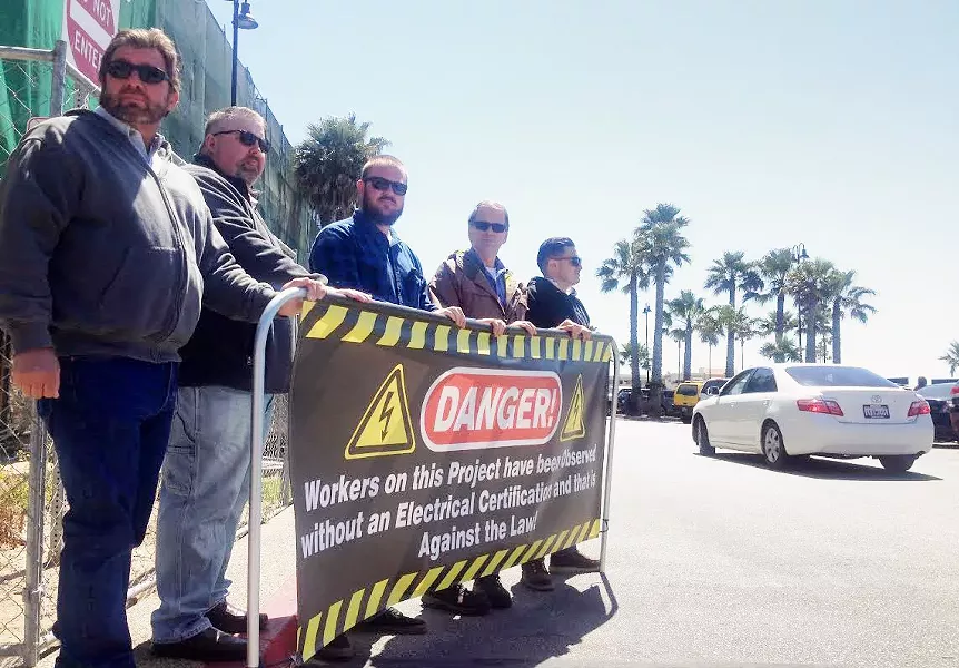IN THE STREETS Members of IBEW Local 639 hold a banner at the construction site of a Pismo Beach hotel to protest the use of uncertified electricians. - PHOTO BY CHRIS MCGUINNESS