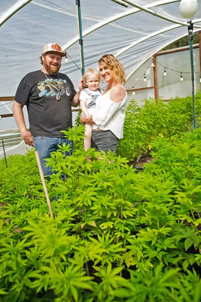 FAMILY FARM Austen Connella (left) and Kristin Kordich (right) pose in front of their Suey Creek cannabis farm with their 3-year-old daughter. - PHOTO BY JAYSON MELLOM