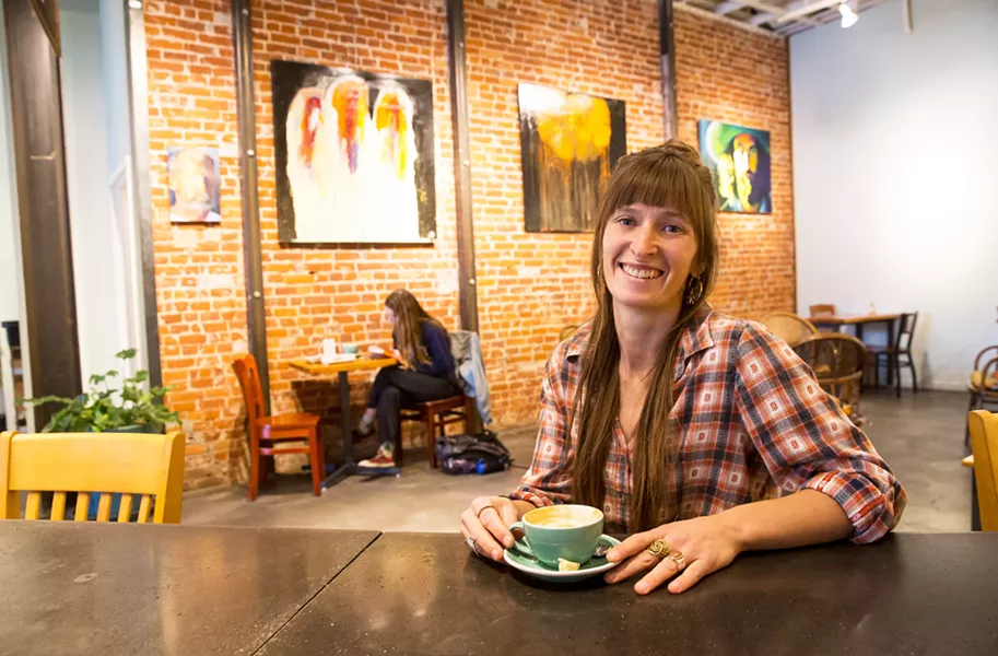 COFFEE SHOP CURATOR Manager and curator for Ascendo Coffee Jenna Madama sips on a coffee in front of the café’s current display of paintings by artist David Zweifel. - PHOTO BY JAYSON MELLOM