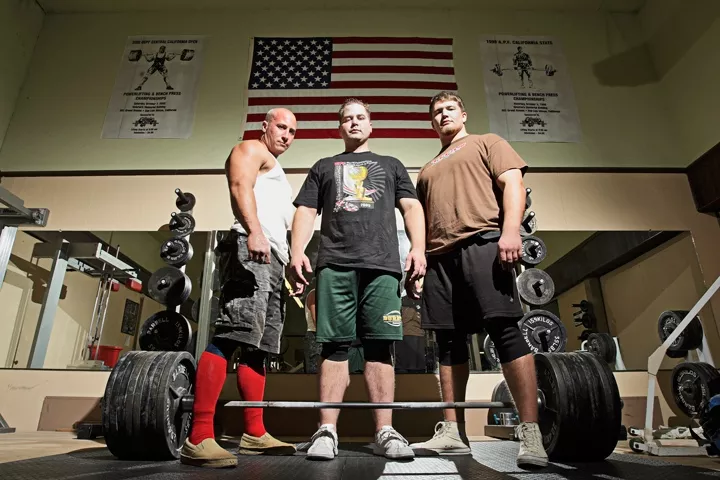 STRONGMEN : Ian Smalley (left), Alan Best, and George Beckham (right) practice heavy metal magic at Estrada’s Gym in SLO; Best stands over a 771-pound bar, his world-record deadlift. - PHOTO BY STEVE E. MILLER