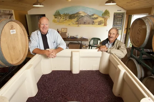 ONCE MILK, NOW WINE: At the old milking barn on the Filipponi Ranch on the outskirts of San Luis Obispo, winemaker Peter Cron and Herb Filipponi showed off a bin of tempranillo grapes that’s about to be pumped into barrels. - PHOTO BY STEVE E. MILLER