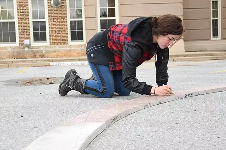 Art student Brittany Standard marks granite pieces for cutting as part of the Coming Together Park sculpture being installed on the USAO campus. mh