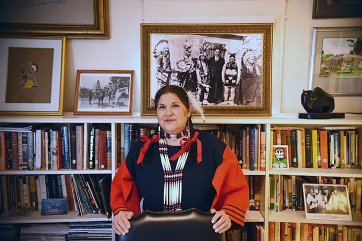 Tracey Satepauhoodle-Mikkanen, executive director of Jacobson House Native Art Center, in the center's cramped office with a historic portrait of the Kiowa Five and Oscar Brousse Jacobson over her shoulder.  The original Kiowa Five included a woman, Lowis Somoky, who steped out and was replaced by James Auchieh.  Officials now refer to the group as the Kiowa Six, puting Smoky back into the group.  2-8-16, at the Jacobson House, 609 Chautauqua Avenue, Norman Oklahoma. - MARK HANCOCK