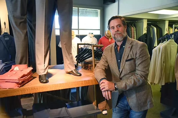 Spencer Stone is wearing a deconstructed blazer made of silk and wool by Isaia, next to mannequins wearing slim pants with little to no break in the hem by Incotex, at his Nichols Hills Plaza store Spencer Stone Company. mh