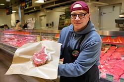 Chris Castelli, meat specialist, poses for a photo with a bone-in rib-eye at Whole Foods. (Garett Fisbeck)