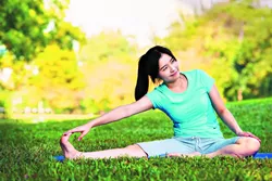 Young woman doing yoga exercise on green grass - BIGSTOCK