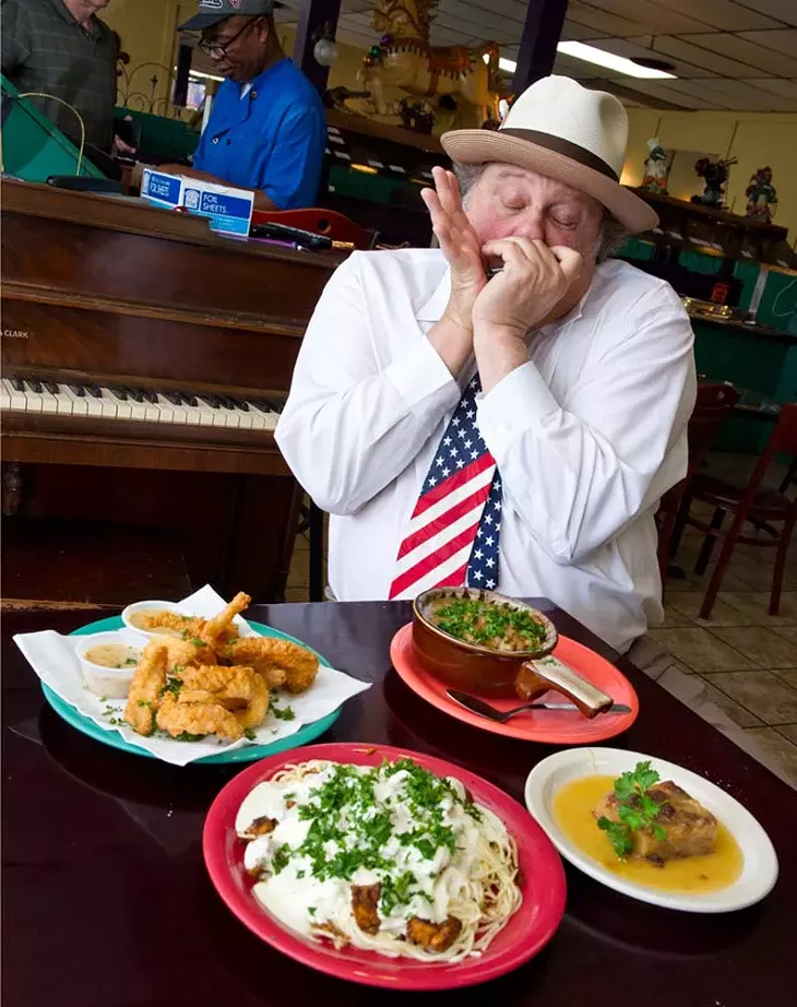 Chicago Dan plays the harmonica at Cajun King regularly. In frony of him sits, fried catfish, etoufe, spicy chicken pasta, and bread pudding. (Shannon Cornman)