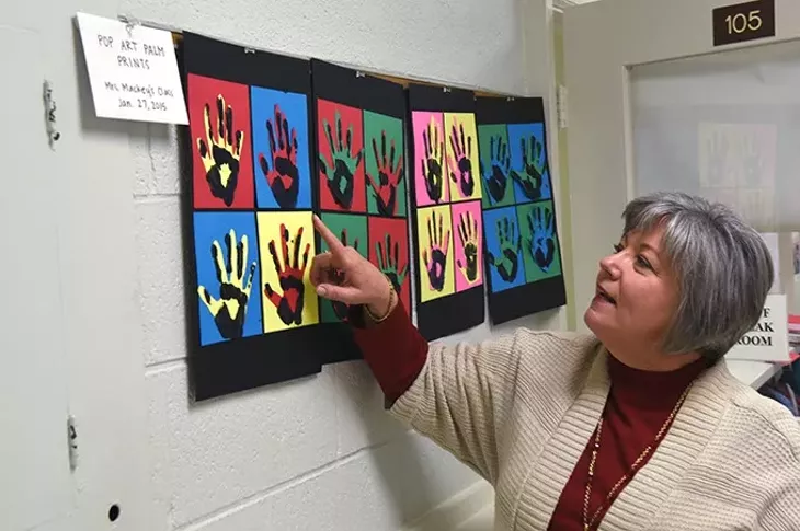Susan Agel, the CEO at Positive Tomorrows, looks over pop art palm prints created by students and displayed in the hallway. mh