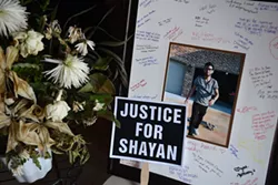 An informal portrait of Shayan Mazroe just getting off his scateboard taken by Mandi Leegard, with signatures and messages from friends, a proped-up yard sign for justice, and a vase of wilted flowers, create a small memorial inside Mandi Leegard's Edmond Home, 10-7-15. - MARK HANCOCK