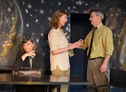 Claire (Angie Duke at center) is excited to share with her husband (Kevin Moore) how visitors are applauding her museum tours now that she is including her religious beliefs, while her boss at the natural history museum (Mary Sue Backus, seated) is very displeased with Claire’s changes. - CARPENTER SQUARE THEATRE / PROVIDED