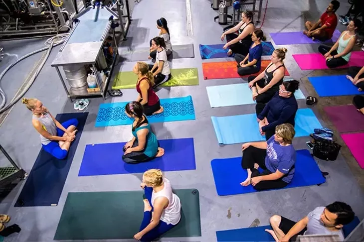 Surrounded by brewing equipment, Instructor Brooke Larson, left, leads a class of Beer Yoga, at Coop Ale Works in southwest Oklahoma City, 10-15-2016. - MARK HANCOCK