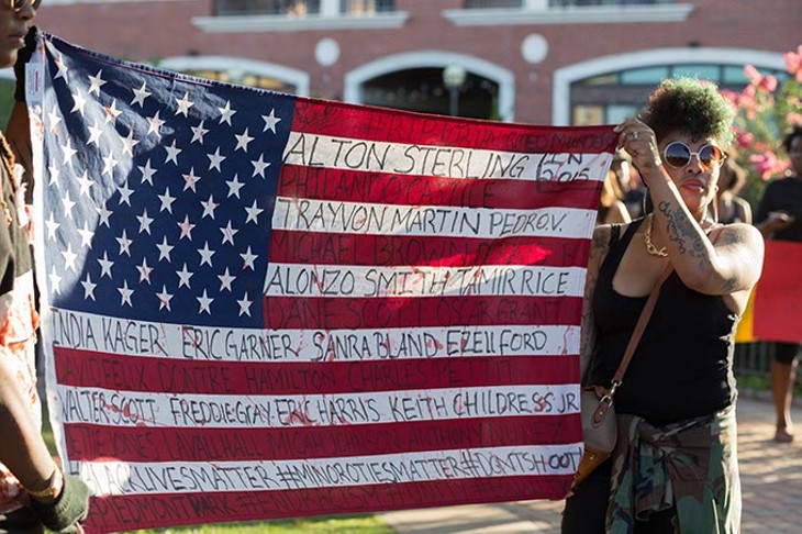 Tyler Watts and wife, April Watts hold up a flag with the names of shooting victims at the Black Lives Matter protest on Sunday, July 10, 2016 in Oklahoma City. - EMMY VERDIN
