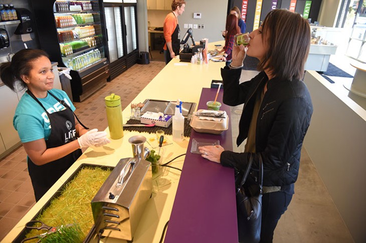 Customer Linsey Liles, at right, does a Wheat Grass Shot, sampling before purchasing, from Victoria Stevenson at the new Organic Squeeze Kitchen Table location in The Edge apartments in MidTown, Oklahoma City, 1-14-16. - MARK HANCOCK