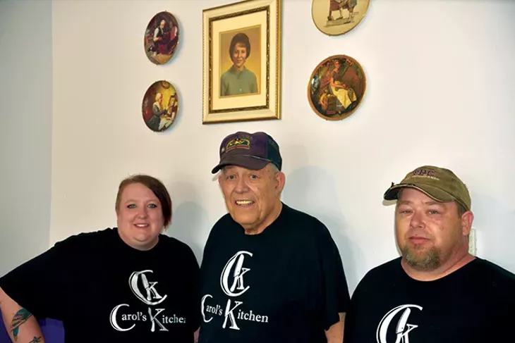 Hailey, Jim and Brian Kahoe stand underneath a photo of Carol Kahoe at Carol’s Kitchen in Norman. - | PHOTO JACOB THREADGILL